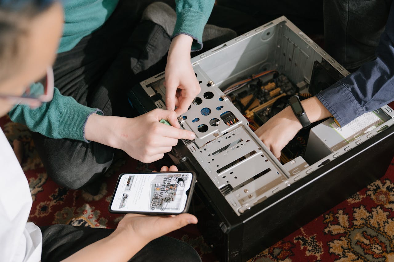 IT-Support in Aktion „IT-Support in Aktion: Zwei Techniker reparieren einen Desktop-PC, während ein Kunde auf dem Smartphone nach technischen Anleitungen sucht.“